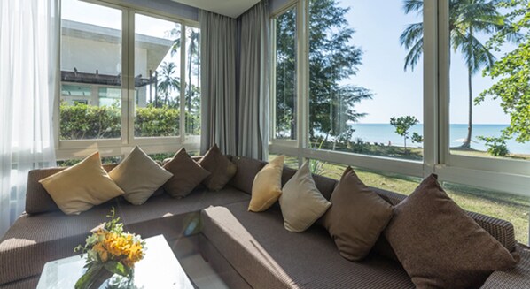 A modern living room with a large sofa, multiple cushions, and a view of the ocean and palm trees. - Kantary Beach Hotel Villas & Suites, Khao Lak (Takua Pa)