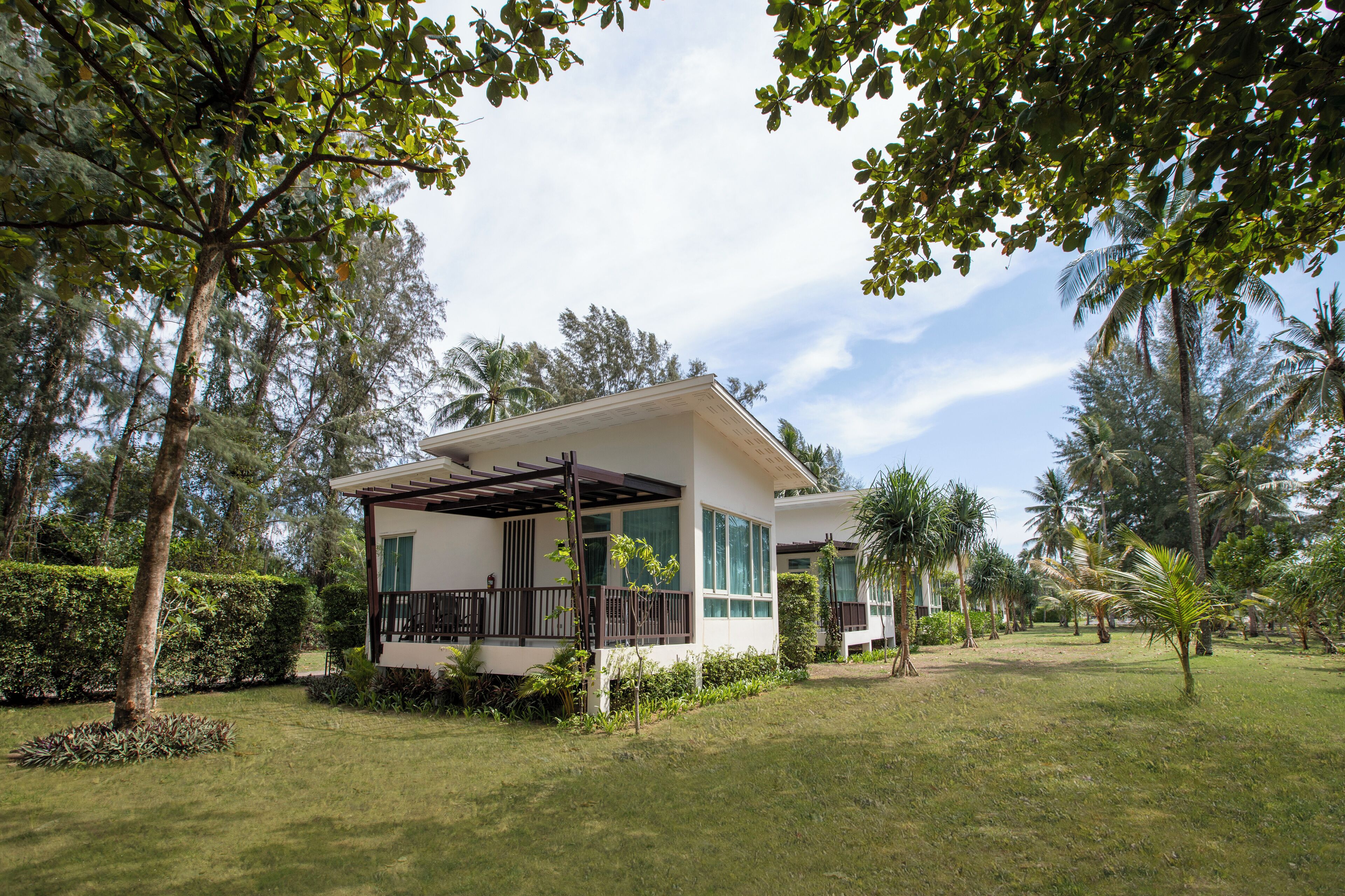 Uma casa de dois andares com varanda coberta, rodeada por vegetação exuberante e palmeiras.