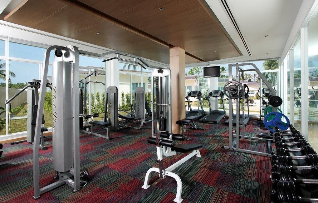 Un gimnasio con diverso equipo de ejercicio, ventanas amplias y vistas al exterior.