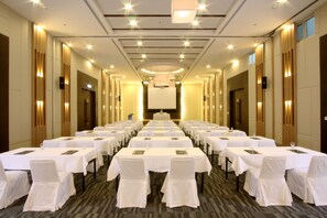 Un salón de conferencias con filas de mesas y sillas, un atril y una pantalla grande al frente.