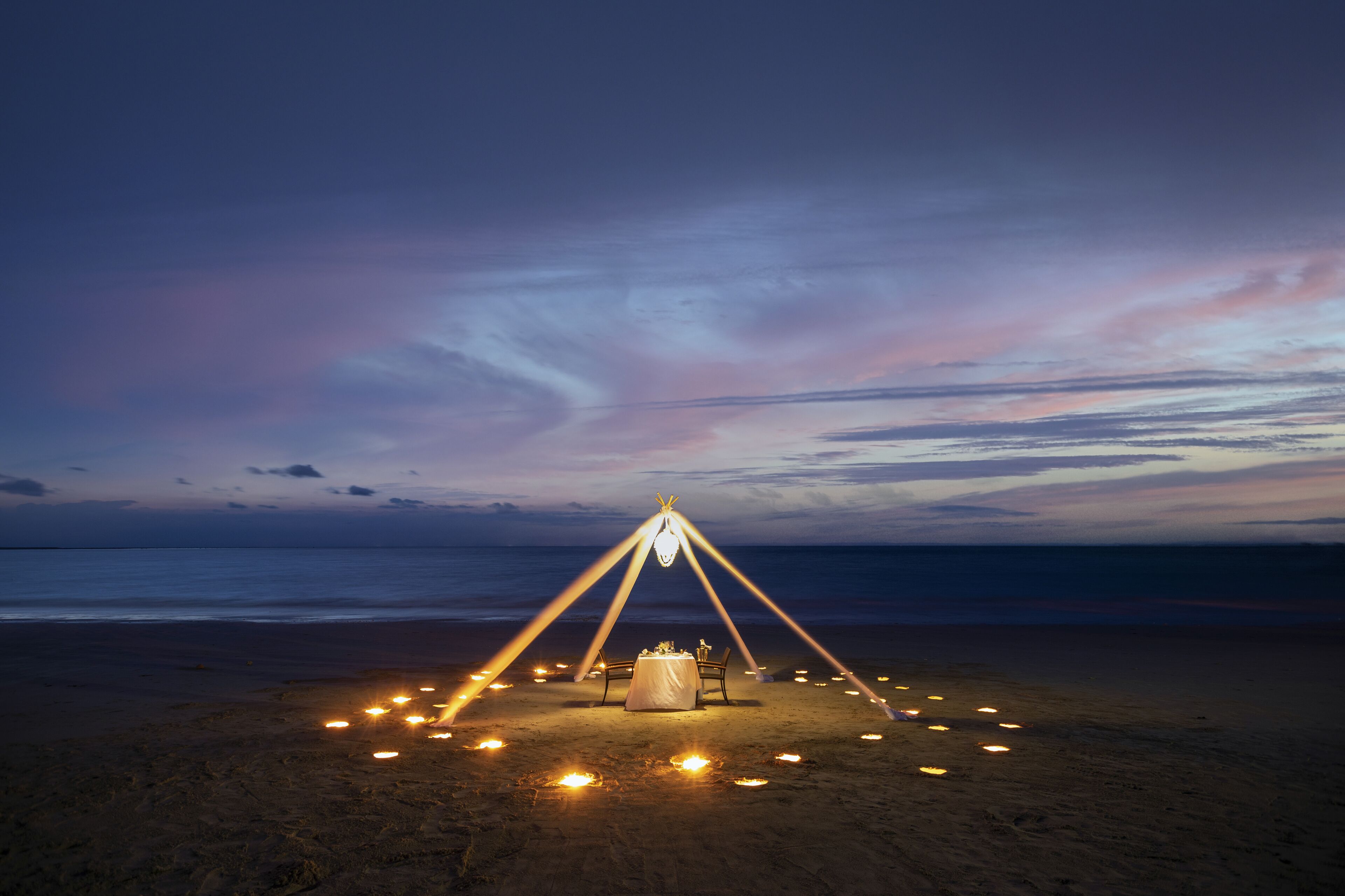 Ein Strandaufbau mit Tisch und Stühlen unter einem Zelt, umgeben von Kerzen.
