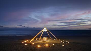 A beach setup with a table and chairs under a tent, surrounded by candles.