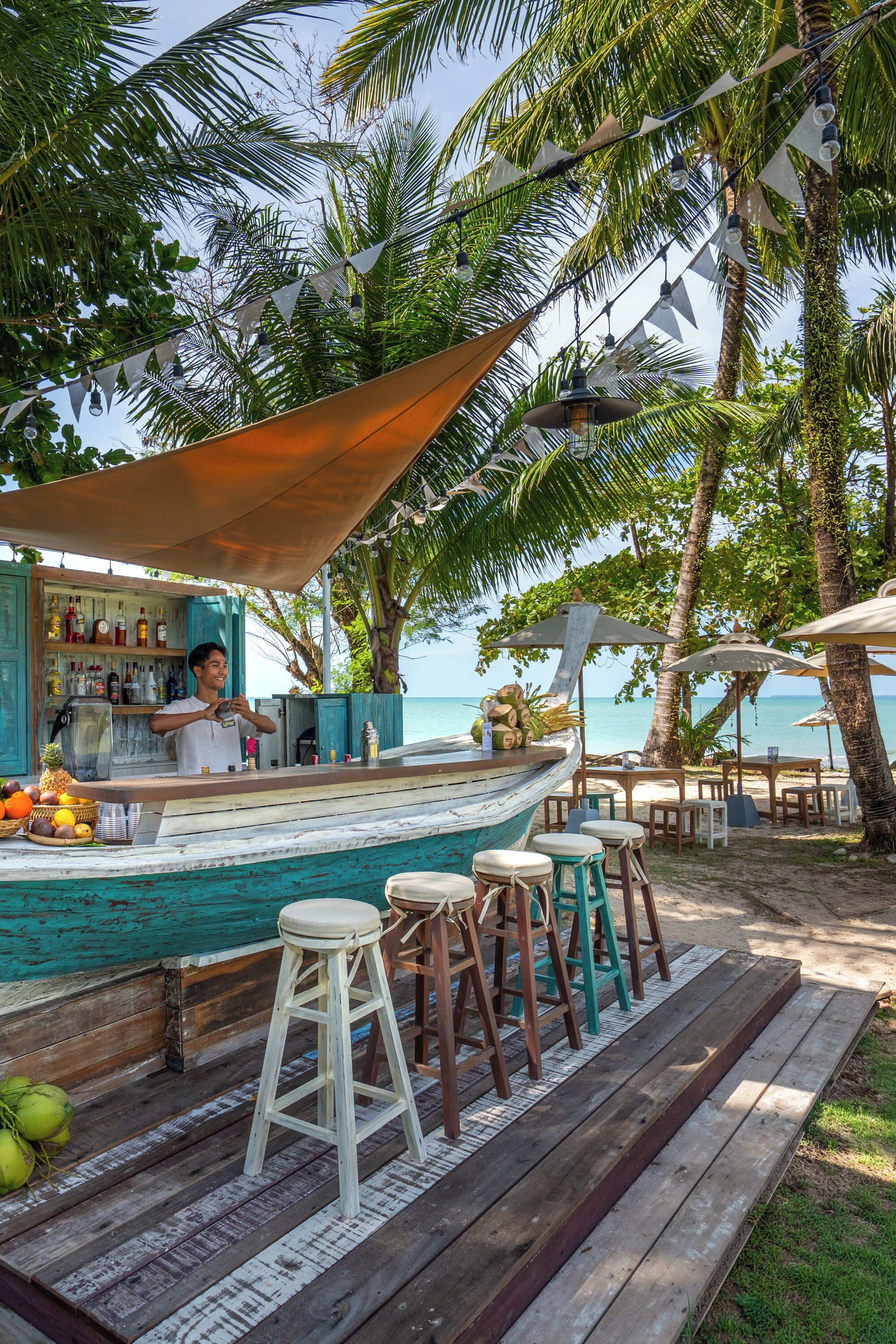 Eine Strandbar mit Holzterrasse, Hockstühlen und einer Bar.