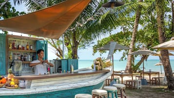 Un bar frente al mar con terraza de madera, taburetes y barra.