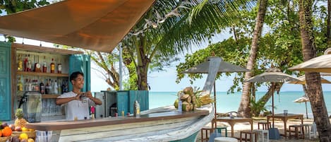 A beachside bar with a wooden deck, stools, and a bar counter.