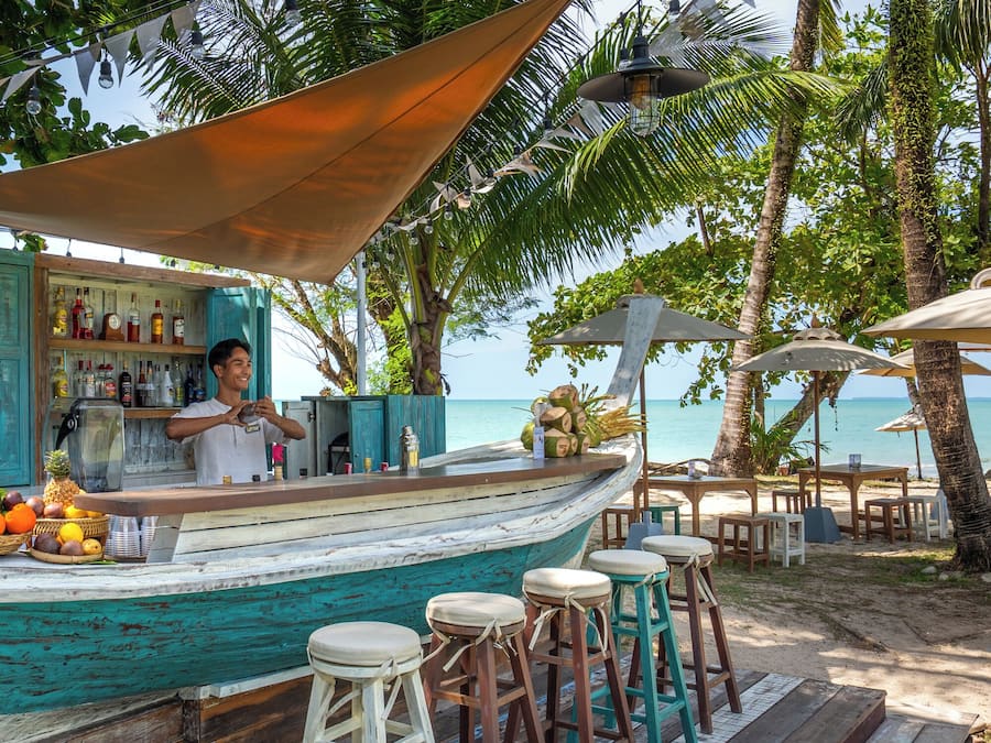 Un bar a la vora de la platja amb terrassa de fusta, tamborets i barra.