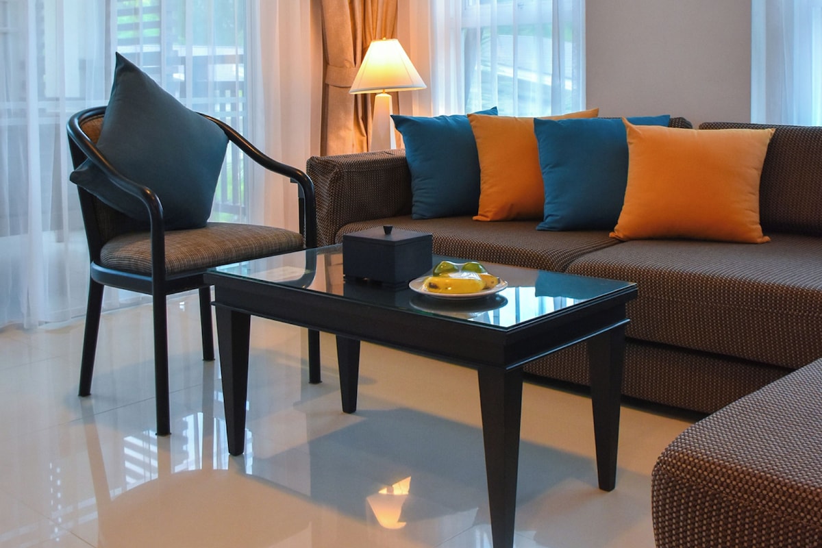 Una suite con amplio salón, un sofá con cojines de colores, una silla, una mesa y una lámpara. La suite tiene una superficie de 58 metros cuadrados y ofrece un espacio habitable generoso con balcones privados amplios y dormitorios separados.