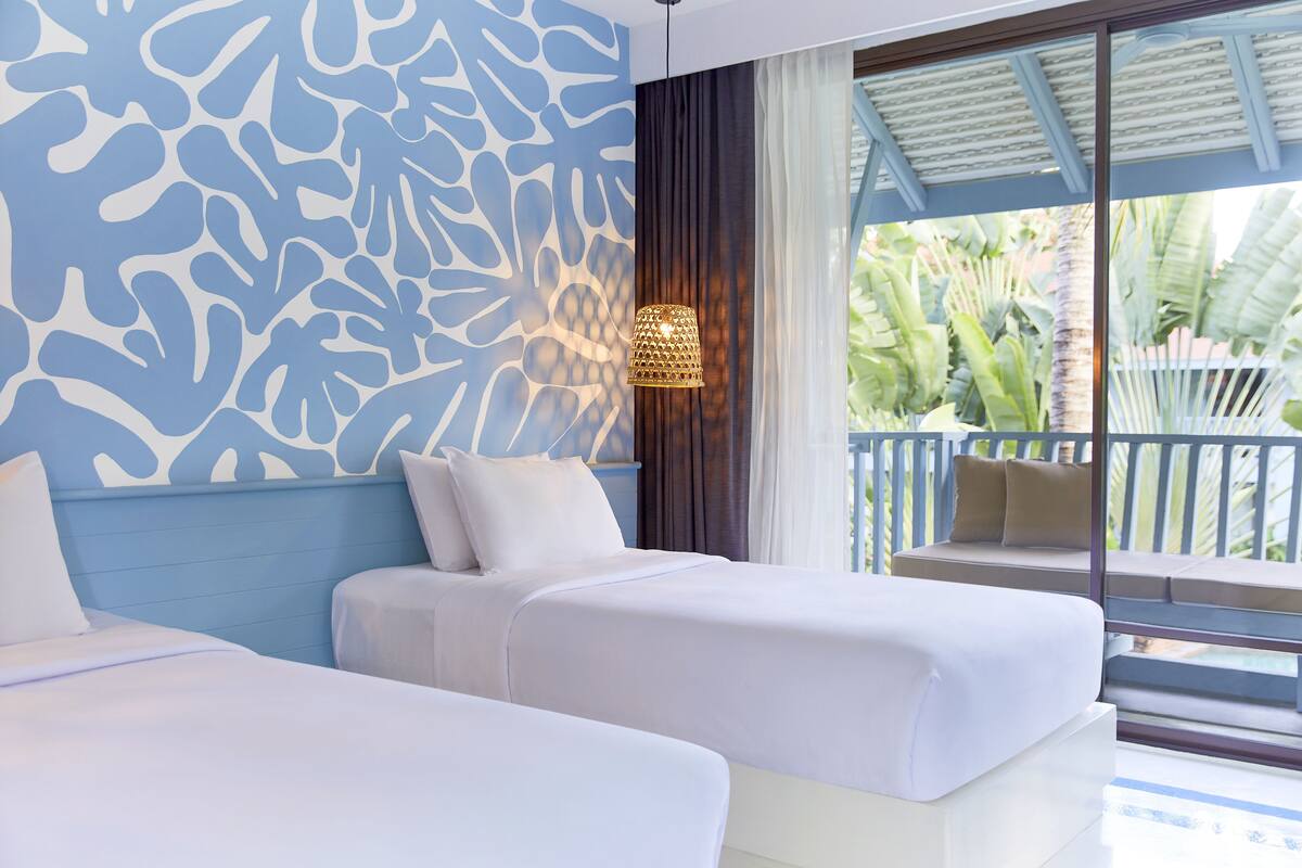 Ein Hotelzimmer mit zwei Betten, einer Wand mit Muster, einer Hängeleuchte und Blick auf einen Balkon mit Sitzgelegenheit.