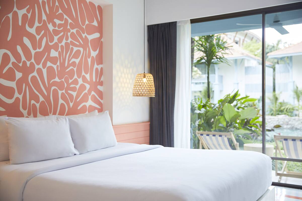 Ein Hotelzimmer mit einem großen Bett, Blick ins Freie und einem mit Vorhängen versehenen Fenster.