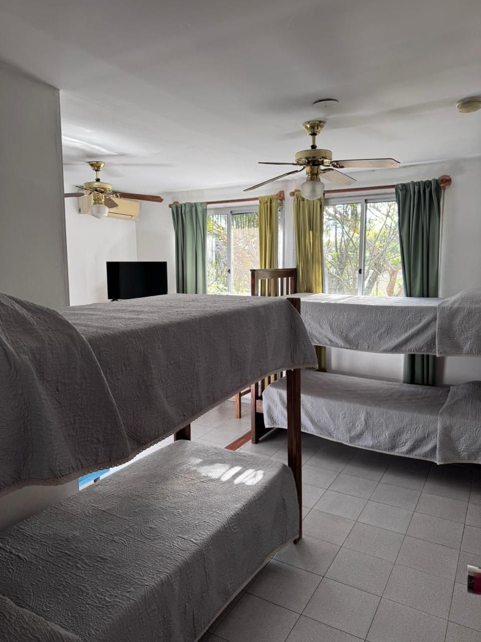 Una habitación con literas, ventilador de techo, televisión y ventana con cortinas.