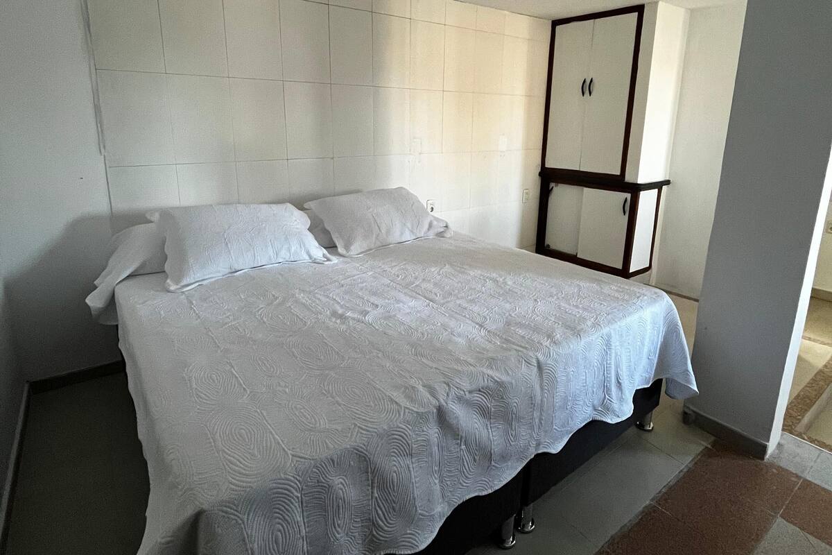 Un lit bien fait dans une chambre d’hôtel, avec une grande tête de lit, une table de chevet et un miroir.