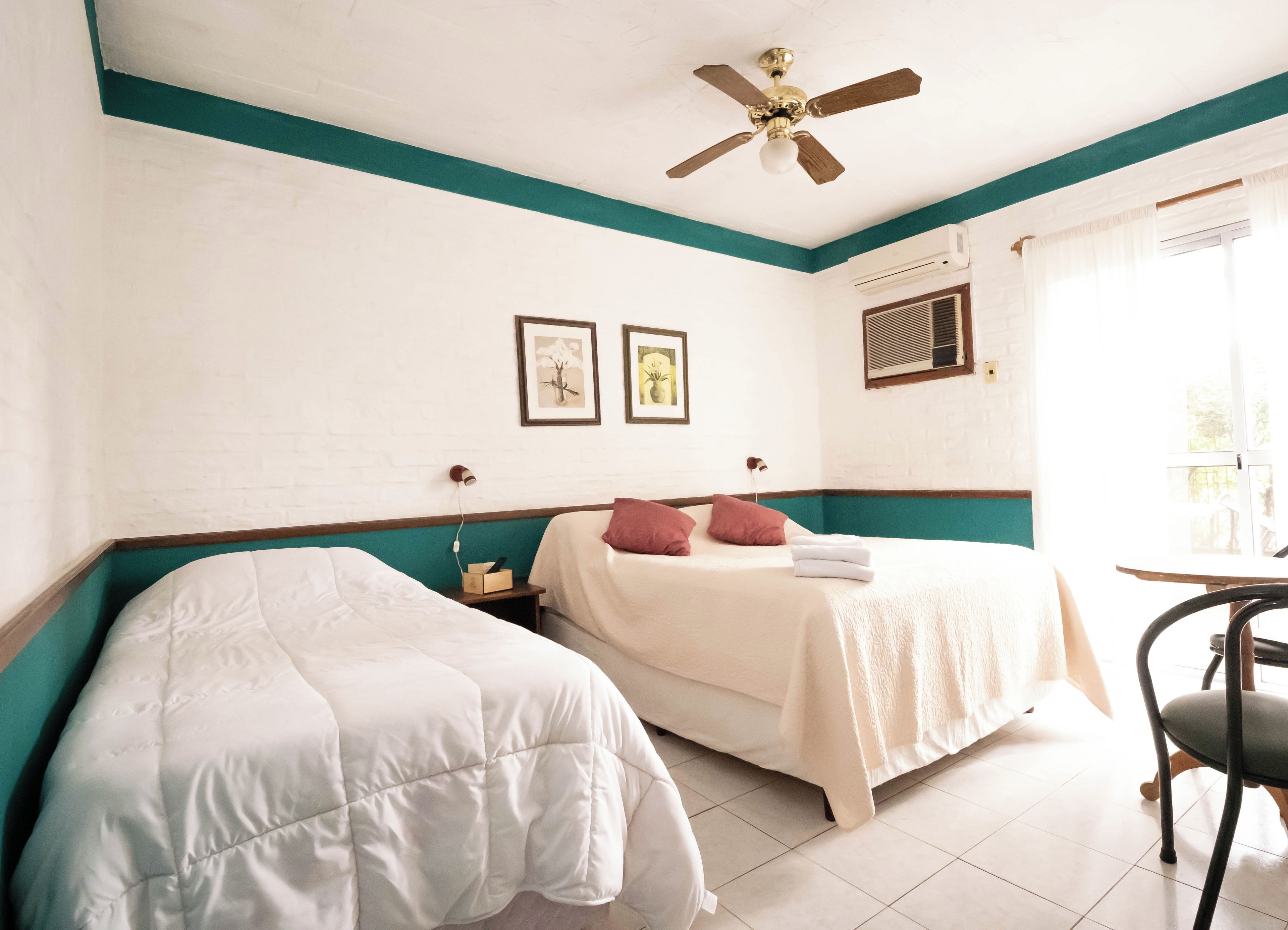 A hotel room with two beds, a ceiling fan, and a window with curtains.