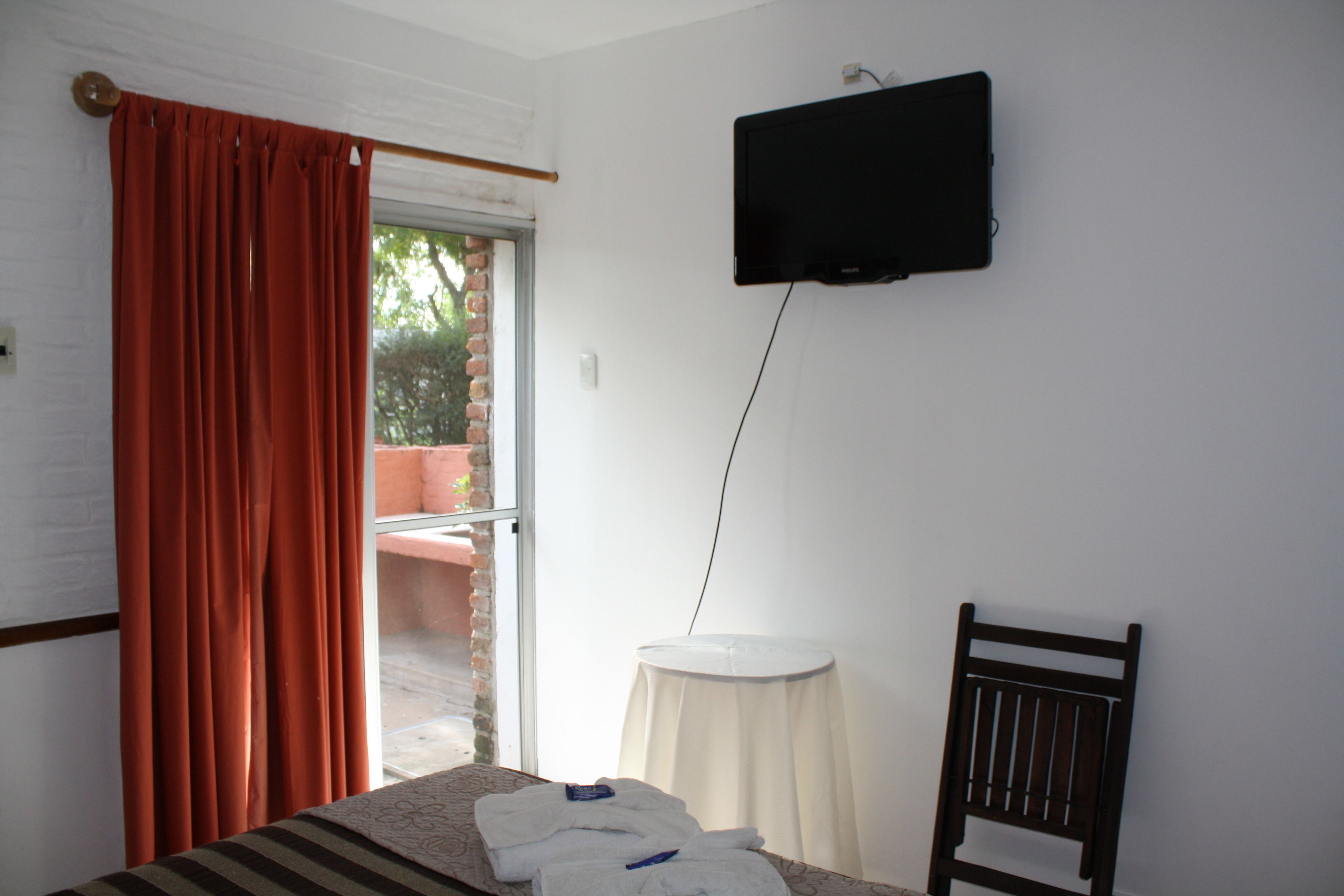 Una camera d'albergo con un letto, una televisione a parete, un tavolino e una sedia.