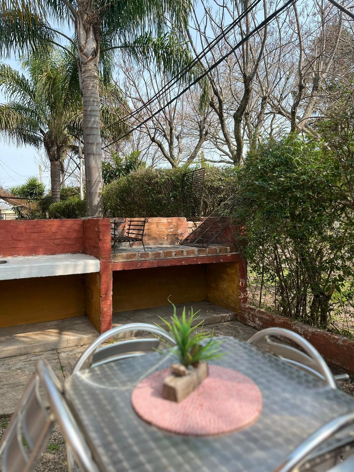 Une terrasse avec une table et des chaises en métal, une petite plante en pot et un mur en briques.