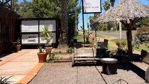 A hotel with outdoor seating, a palm tree, and a thatched-roof structure.