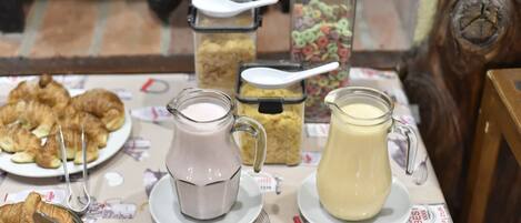 A breakfast table with croissants, two pitchers of milk, and cereal containers.