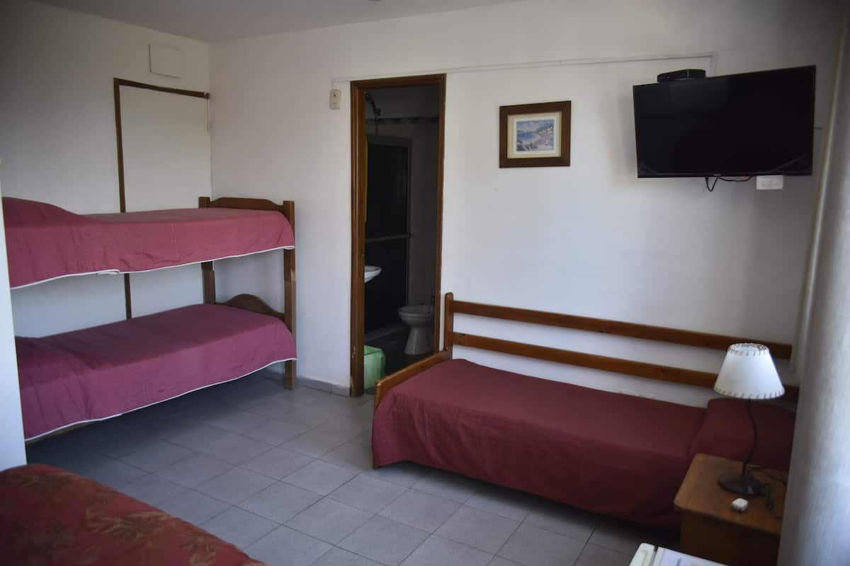 A dormitory room with bunk beds, a television, a bedside lamp, and a bathroom door.