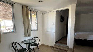 A room with a bed, a small table with two chairs, a window with curtains, and a staircase leading to another room.
