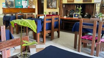 Interior de restaurante con sillas de madera, una mesa con mantel oscuro y un florero con planta.