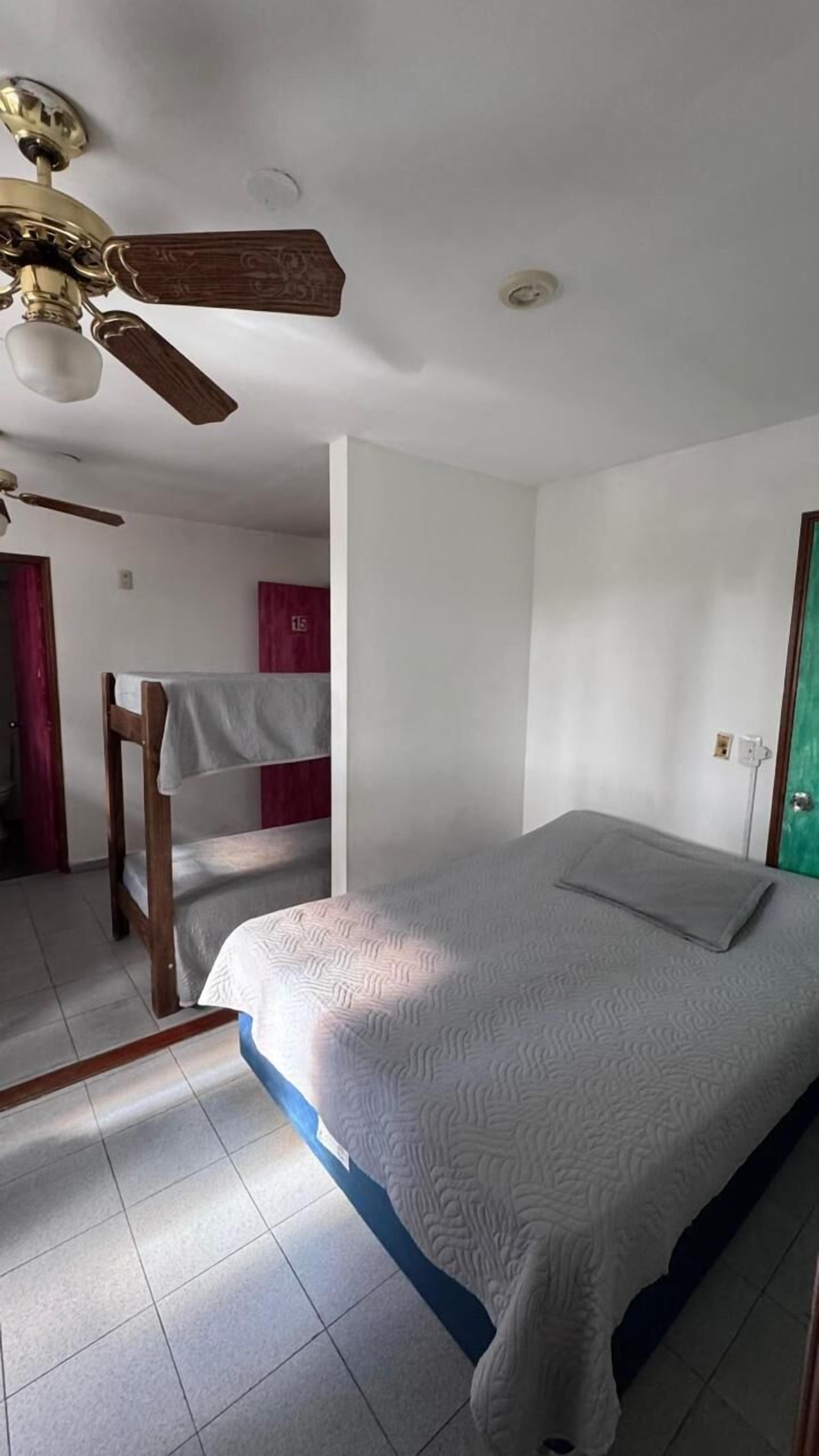 A bedroom with a bed, a wooden chair, a ceiling fan, and a door.