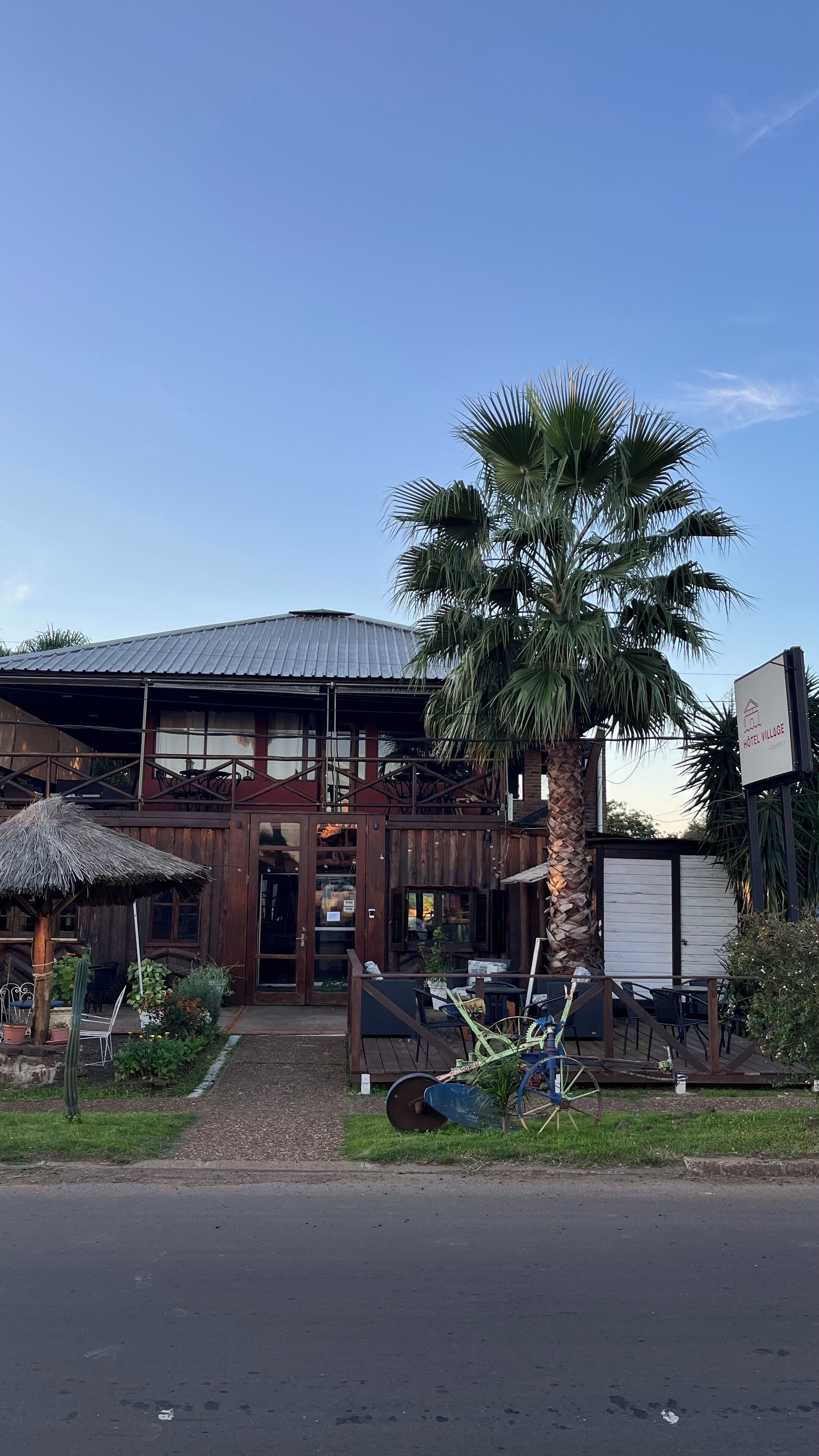 Un edificio rustico con tetto in metallo, veranda in legno e una palma davanti.