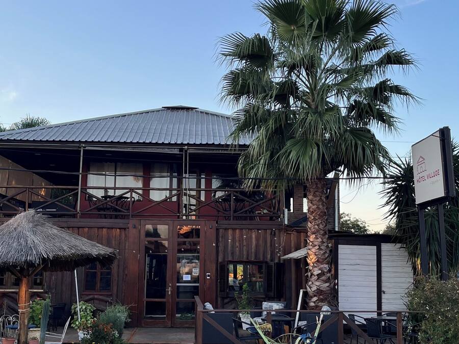 Un edificio rustico con tetto in metallo, veranda in legno e una palma davanti.