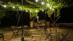 An outdoor patio area with tables and chairs, covered by a pergola with string lights.