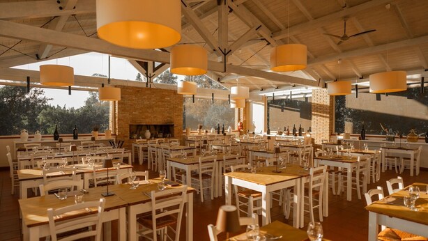 A spacious dining area with multiple tables and chairs, large hanging lamps, and a brick fireplace.