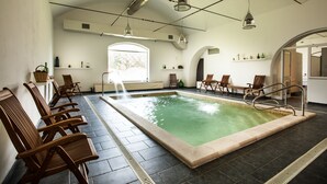 A swimming pool with chairs and a bench, a window, and a door leading to another room.
