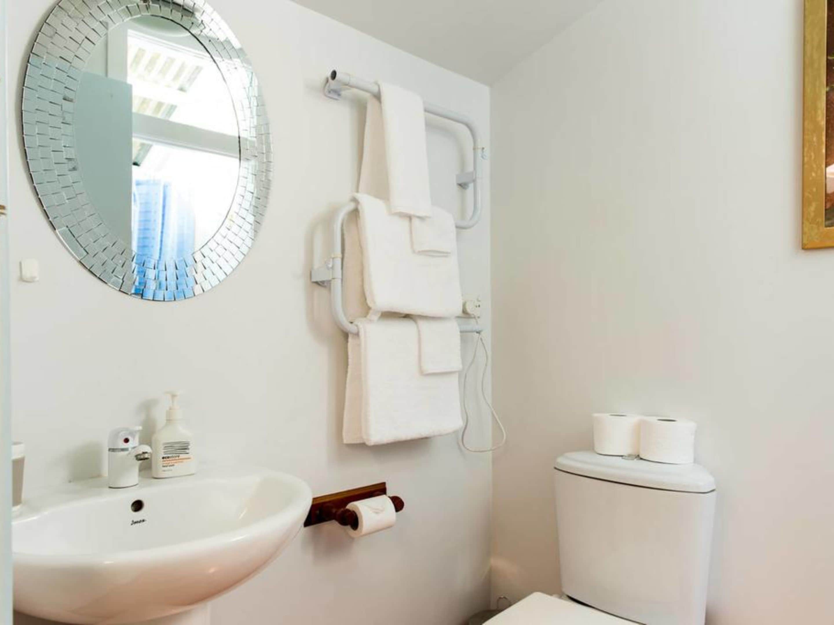 A bathroom with a sink, mirror, towel rack, toilet, and toilet paper.