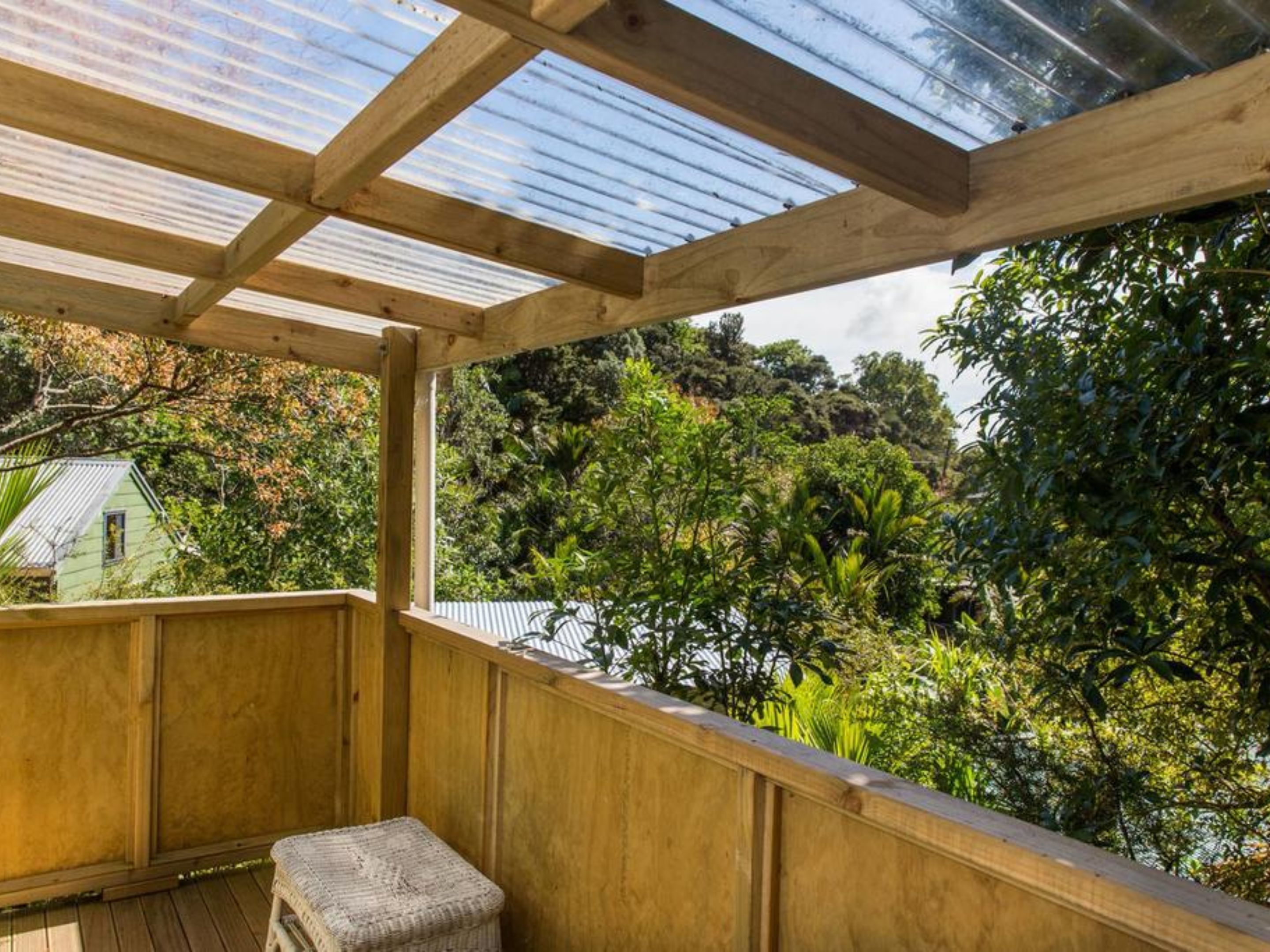 A wooden deck with a glass ceiling, overlooking a lush garden and a house in the background.