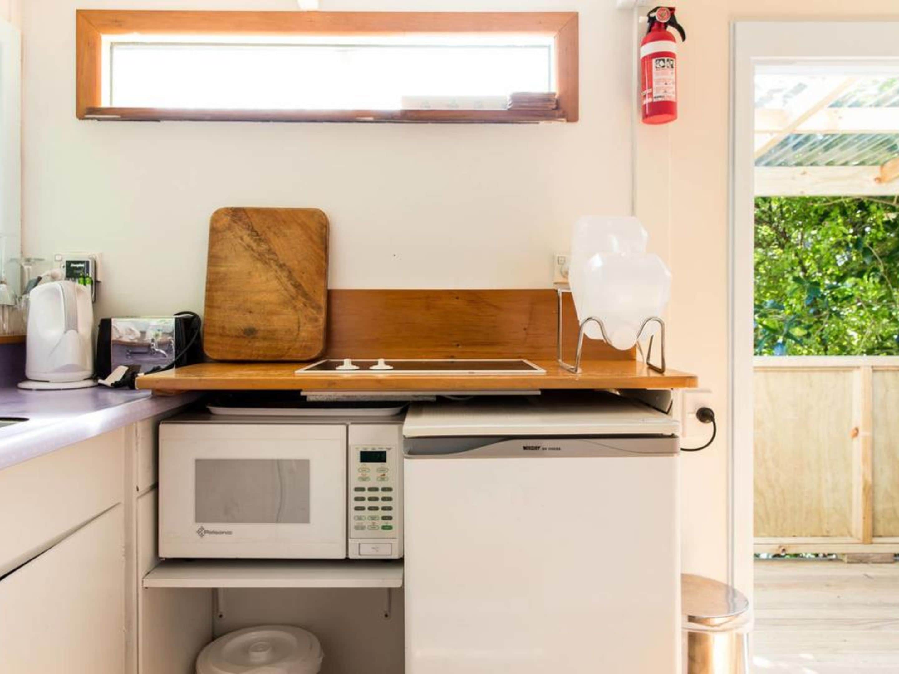 A compact kitchenette with a microwave, a wooden cutting board, and a white chair.