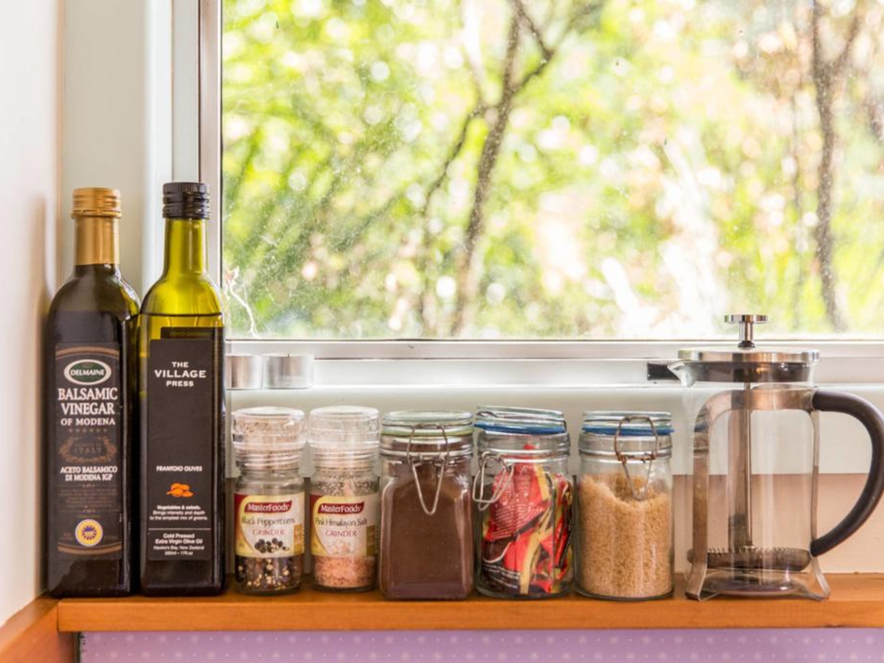 Un alféizar con botellas de vinagre balsámico, un prensador y diversas especias y granos.