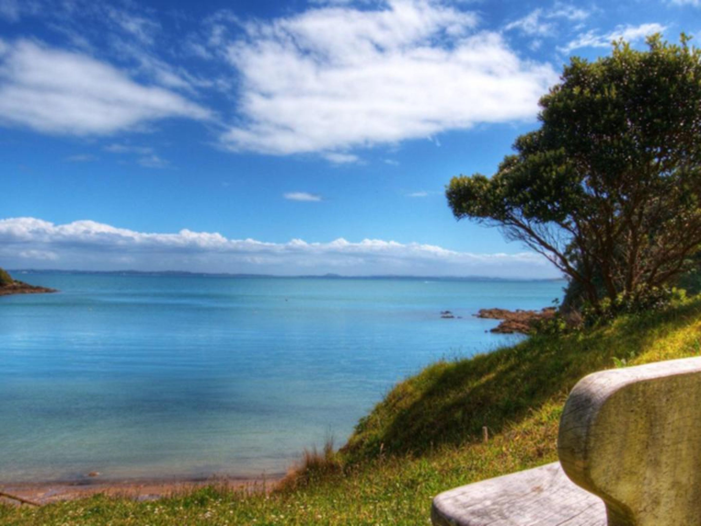 A bench overlooking a calm sea with a clear sky.