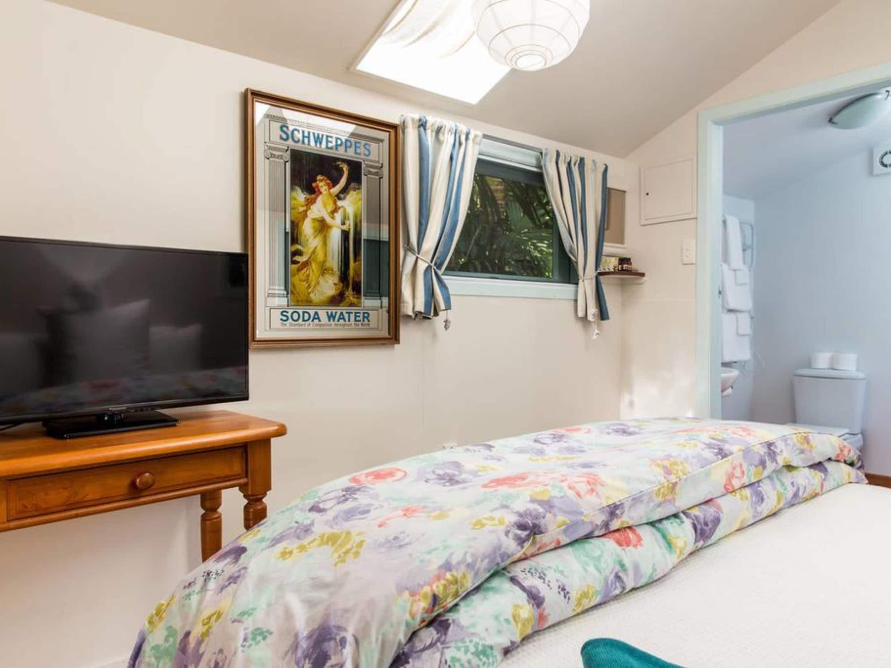 A bedroom with a bed, a television on a wooden table, a poster on the wall, and a window with curtains.