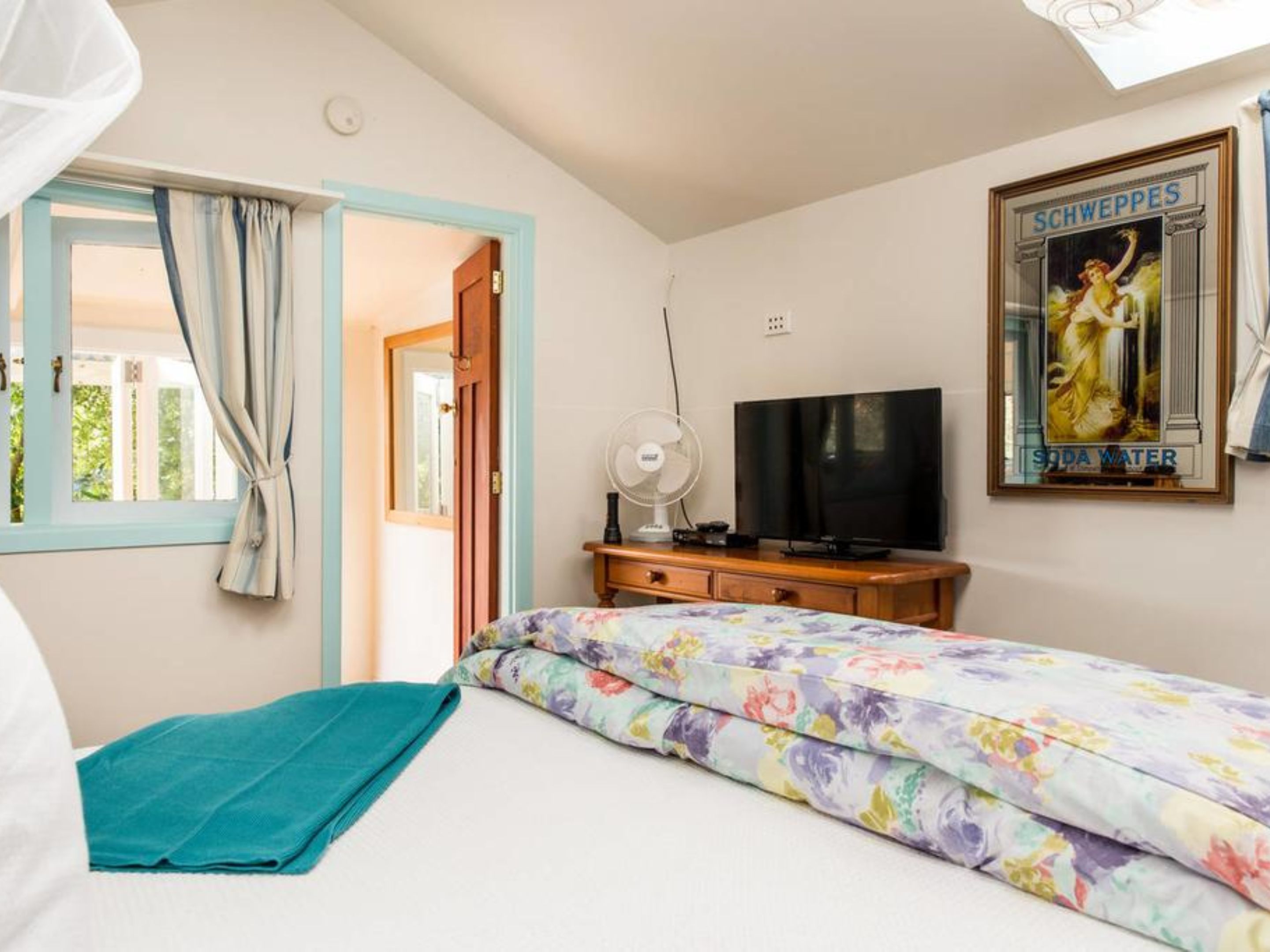 A bedroom with a bed, a TV, a fan, and a poster on the wall.