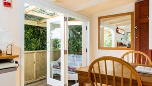 Une table de salle à manger en bois, accompagnée de chaises, une porte blanche donnant sur un espace extérieur abrité et un extincteur fixé au mur.