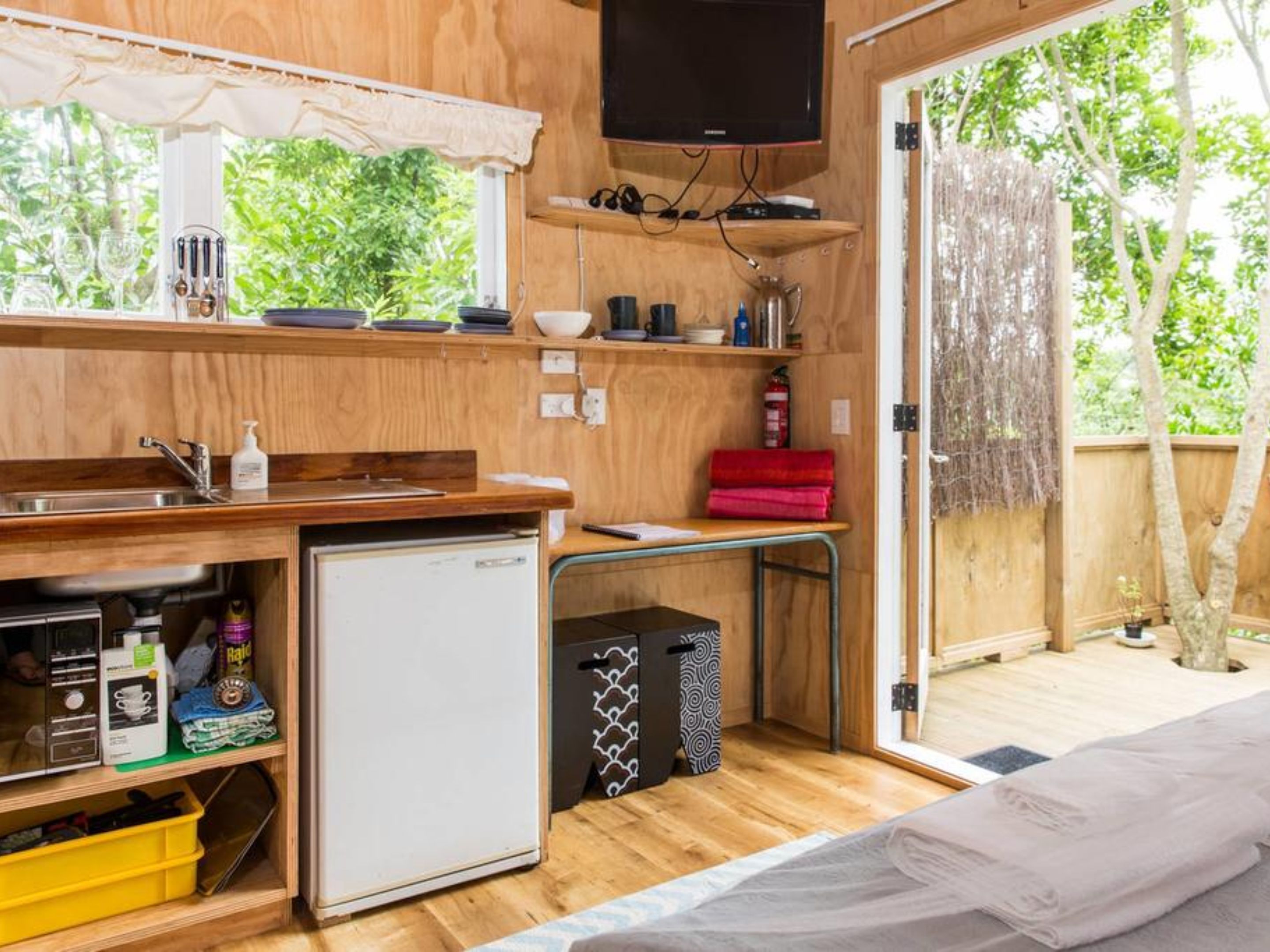 A compact kitchen with a sink, a small refrigerator, and a microwave. There is a wooden countertop with various items and a television mounted above it.
