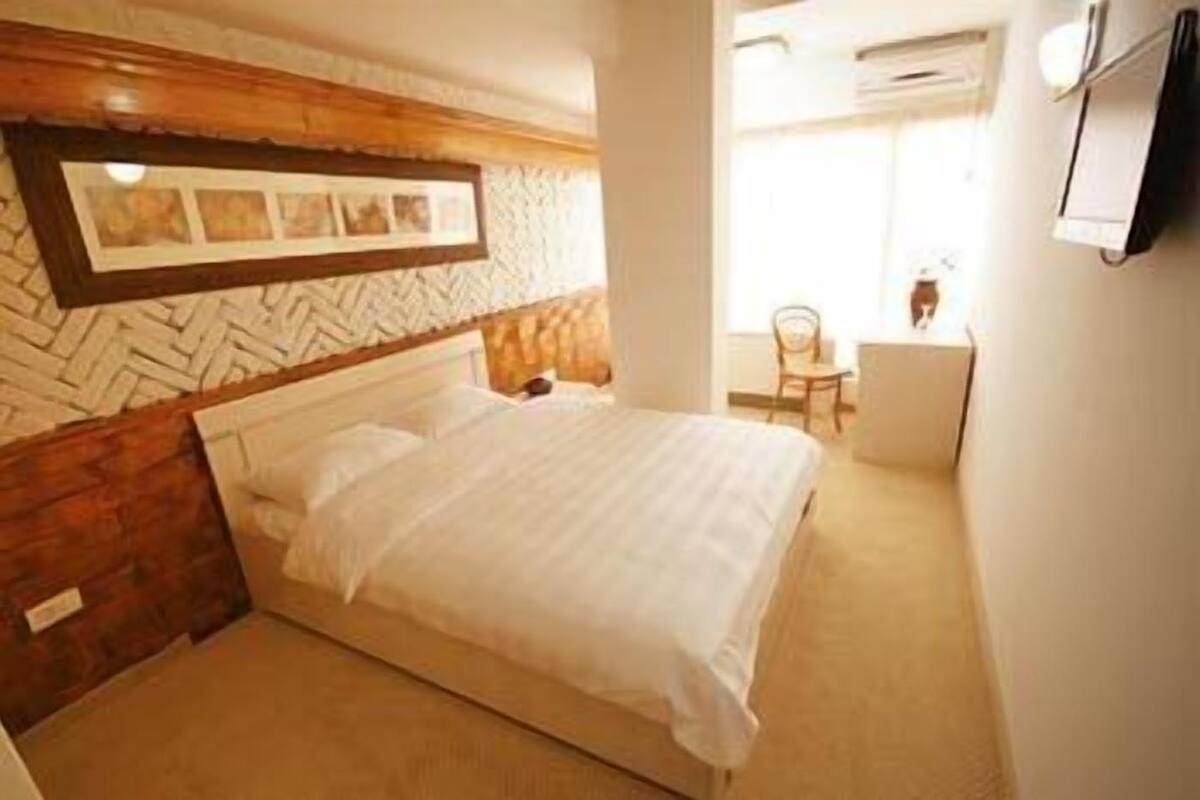 Un dormitorio con cabecera de madera, una cama con ropa de cama blanca, un escritorio pequeño y una silla.