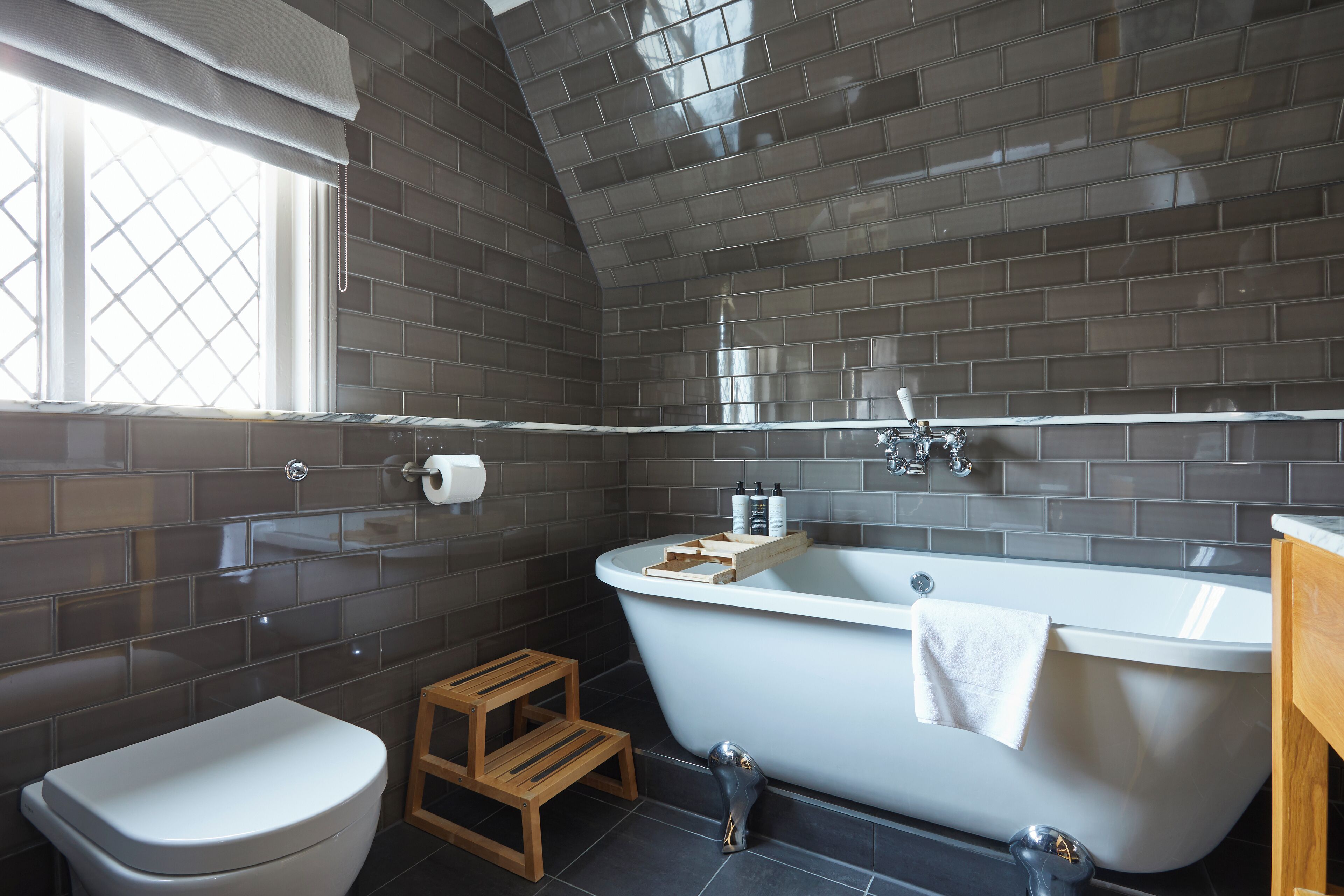 A modern bathroom with a freestanding bathtub, a toilet, and a wooden stool.