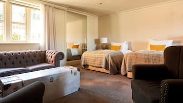 A hotel room with a large window, a sofa, two beds, a chair, and a suitcase.