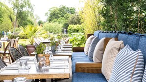 An outdoor dining area with wooden tables and blue upholstered seating. - The Great House, Sonning, Berkshire (Reading)