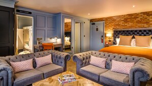 A hotel room with a large bed, two tufted sofas, a coffee table, and a desk with a chair. - The Great House, Sonning, Berkshire (Reading)