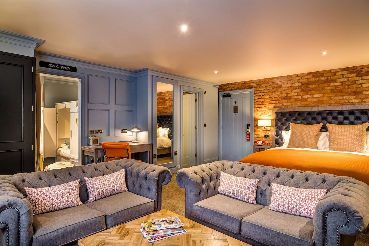 Una habitación de hotel con una cama grande, dos sofás capitonados, una mesa de centro y un escritorio con silla.