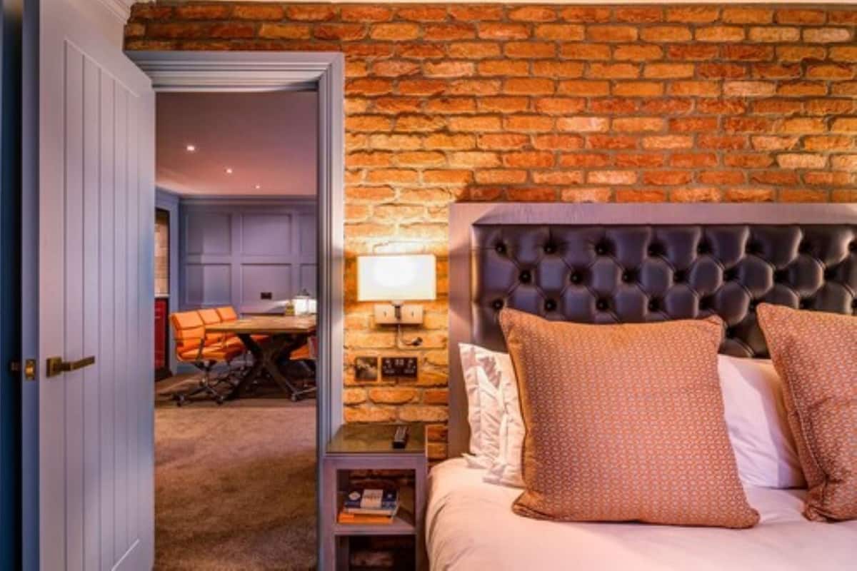 Un dormitorio con pared de ladrillo, cabecera capitonada y cama con almohadas estampadas.