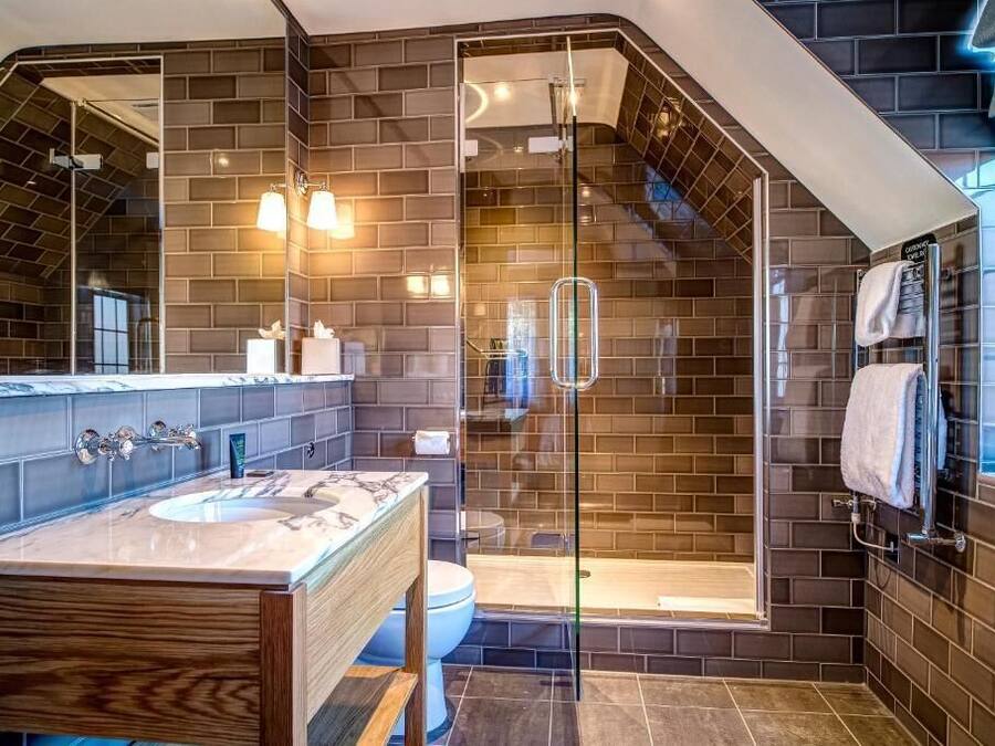 A modern bathroom with a large mirror, a wooden vanity, a glass-enclosed shower, and dark tiled walls.