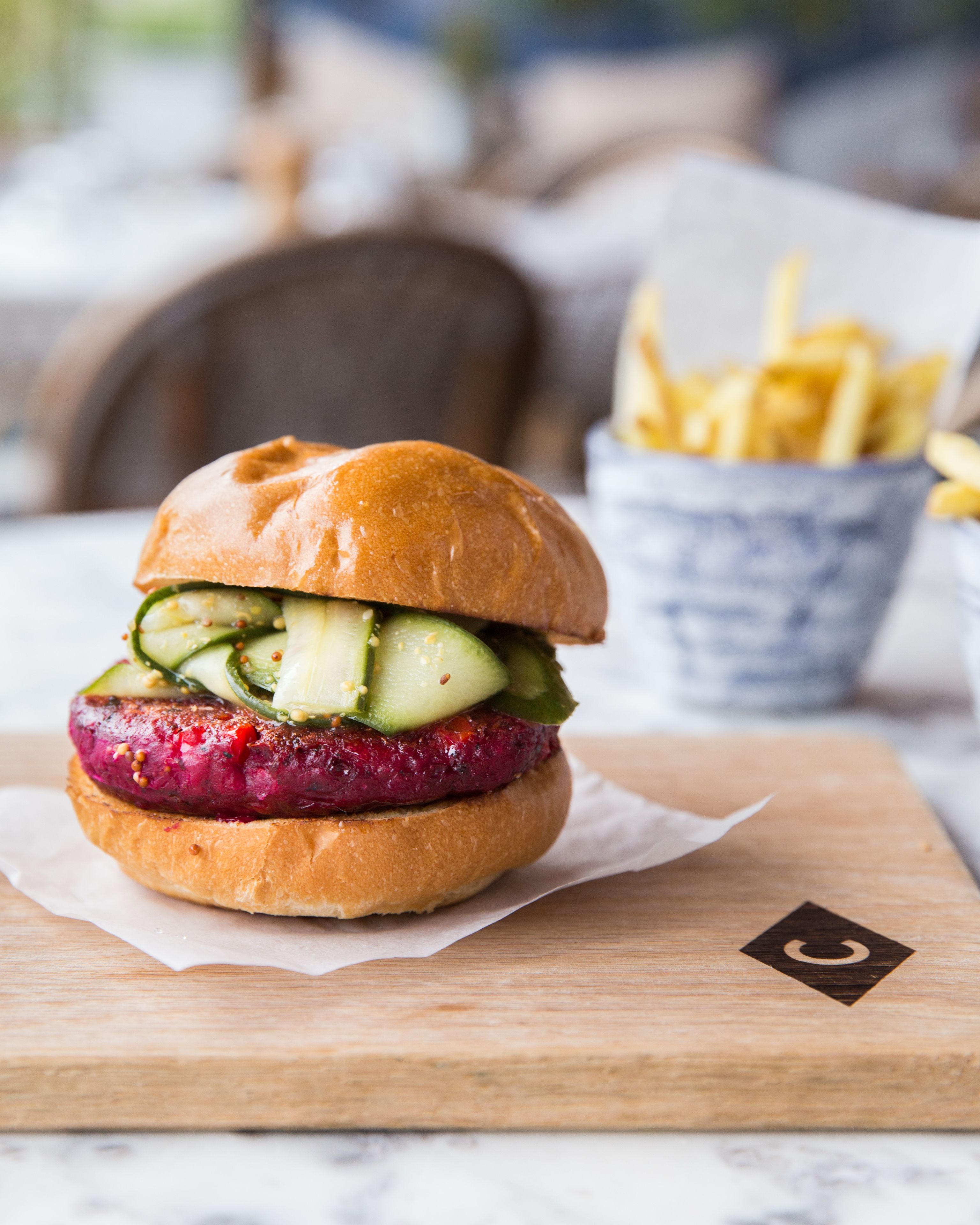 Una hamburguesa con pan, una loncha de carne y una rodaja de pepino sobre una tabla de madera.