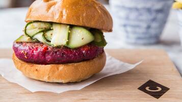 Una hamburguesa con pan, una loncha de carne y una rodaja de pepino sobre una tabla de madera.