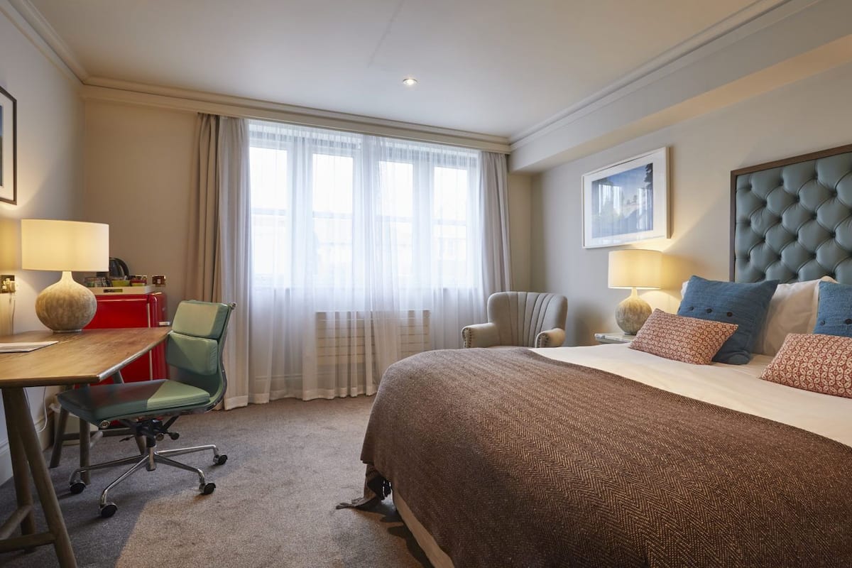 Una habitación de hotel con una cama grande, un escritorio, una silla y una ventana con cortinas translúcidas.
