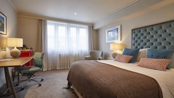 Een hotelkamer met een groot bed, een bureau, een stoel en een raam met dunne gordijnen.